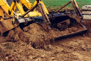 A close-up excavator loads soil into the bucket for further driveway installation.