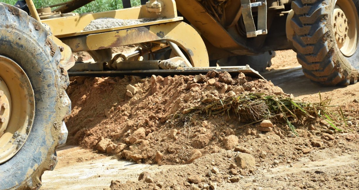 A pile of soil with blade of motor grader machine work for clearing ground level before soil filling for making to rural road.